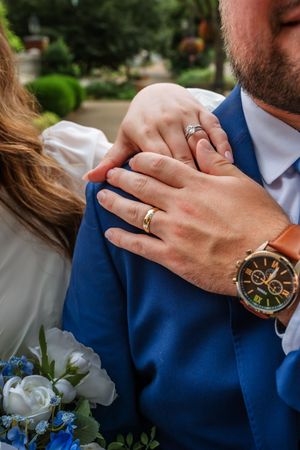 Close-up wedding detail shots of rings, watches and hands against blue suit backdrop.