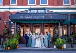 Wedding party poses in front of the historic Blennerhassett Hotel entrance with blue awning and potted plants.