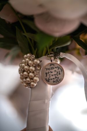 A pearl bracelet with decorative charm attached to a white wedding bouquet wrap.