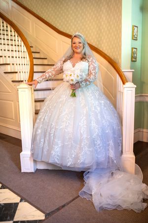 A bride in a full lace ballgown poses elegantly on a curved staircase.