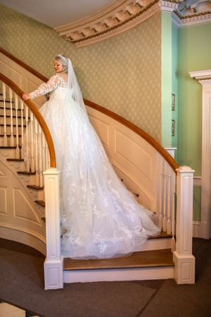 An elegant wedding dress with lace details and long train displayed on a curved wooden staircase.