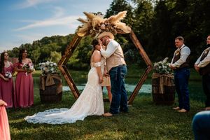 Outdoor wedding celebration with guests gathered on a grassy hillside under blue summer skies.