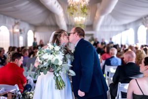 A wedding reception under a white tent with guests mingling and floral centerpieces adorning the tables.
