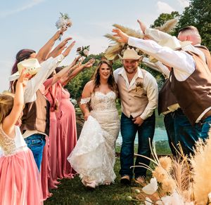 Wedding party celebrates on grassy lawn near lake with vintage decor and coral colored dresses.