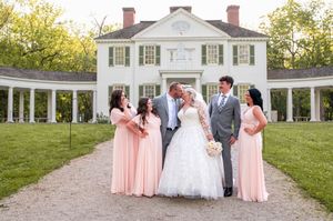 Wedding party poses in front of a historic white colonial mansion with bridesmaids in pink dresses.