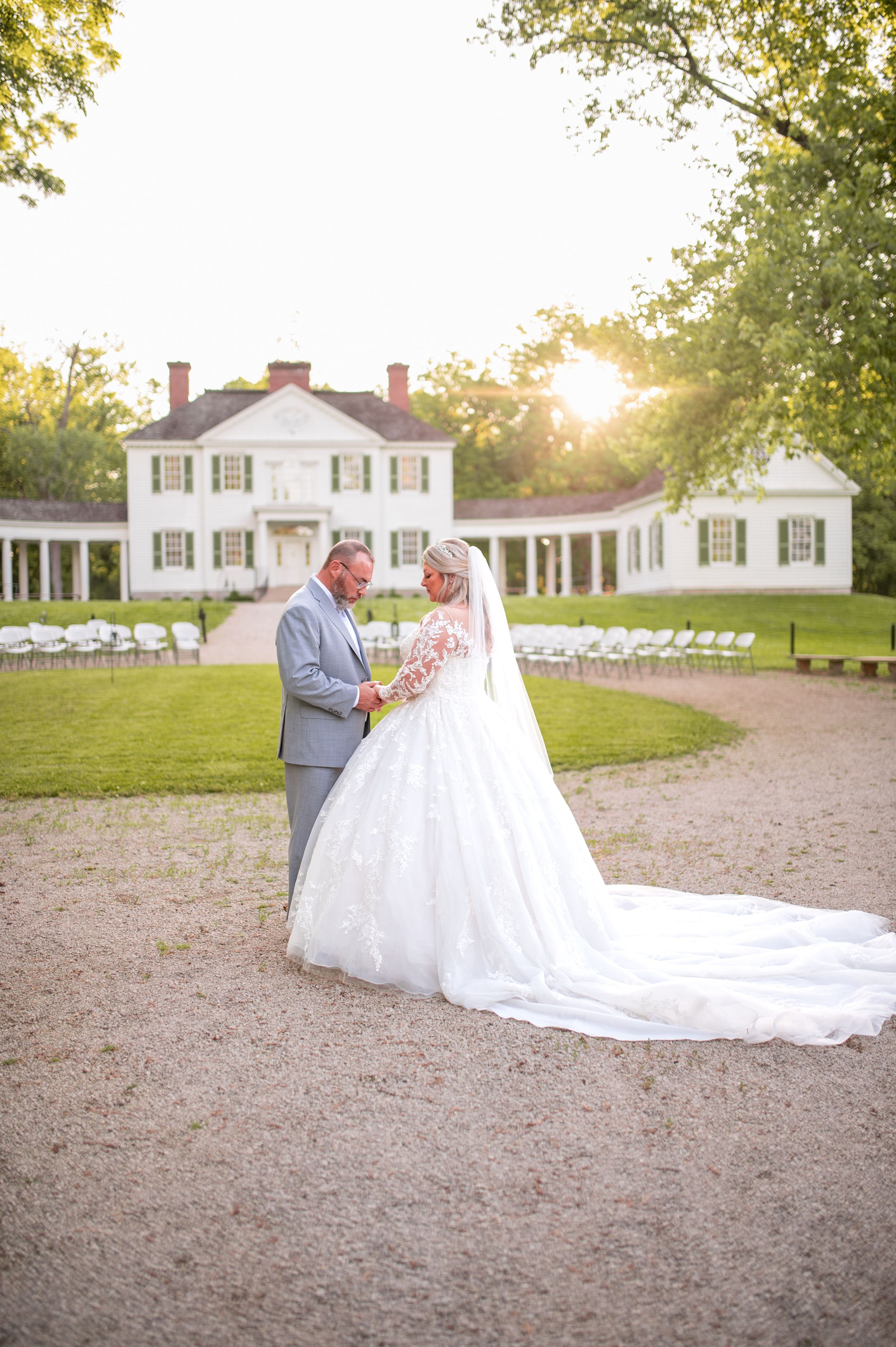 Newlyweds share a moment at sunset in front of a white colonial mansion with curved colonnades.