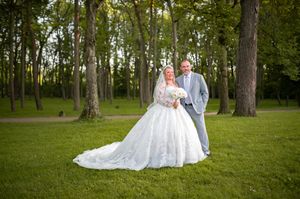 A wedding couple poses in a wooded setting wearing formal attire.