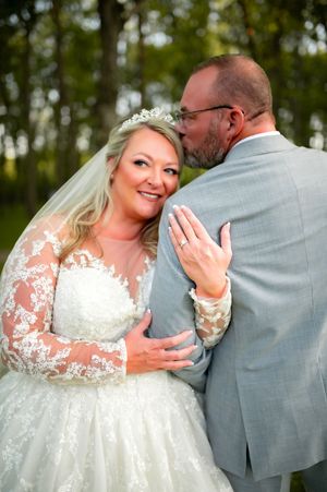 A tender moment between newlyweds in formal attire captured in an outdoor setting.