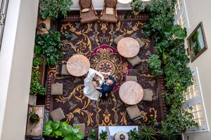 Aerial view of a decorative courtyard with ornate floor pattern, round tables and lush green plants along the walls.