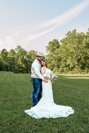 Dancing couple share intimate moments on a sunny lawn surrounded by green trees during wedding photoshoot.