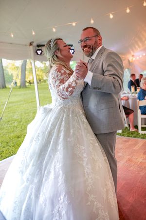 Joyful couple sharing their first dance under string lights in a wedding tent.