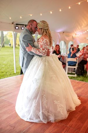 Newlyweds dance together under twinkling lights in an outdoor reception tent.