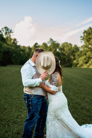 Romantic couple embracing in a sun-lit green field during their country wedding photoshoot.