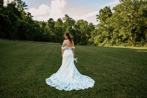 Beautiful wedding dress with flowing lace train spreads across a lush green lawn during a sunny summer day.