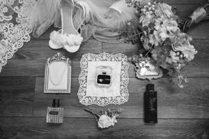 Wedding accessories flat lay including shoes, rings, perfume and floral elements in black and white.