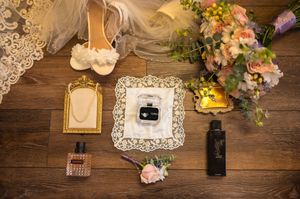 Wedding day details arranged on rustic wooden table with vintage frames, lace doilies and floral bouquets.