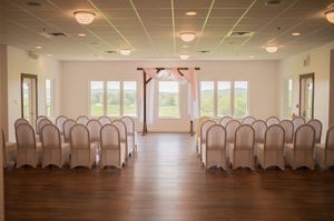 An elegant wedding ceremony space with rows of white-covered chairs and soft natural lighting.