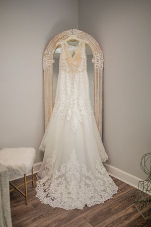 An elegant lace wedding dress displayed on a hanger in an ornate vintage-style mirror.