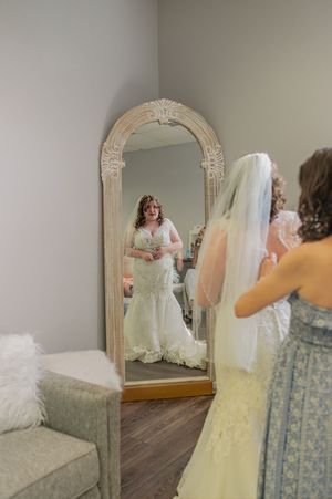 A wedding dress reflection in an ornate floor mirror during bridal preparations.