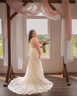 A bride poses with bouquet under pink drapery in a sunlit venue room.