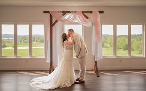 A romantic moment captured under a draped arch with natural light streaming through panoramic windows.