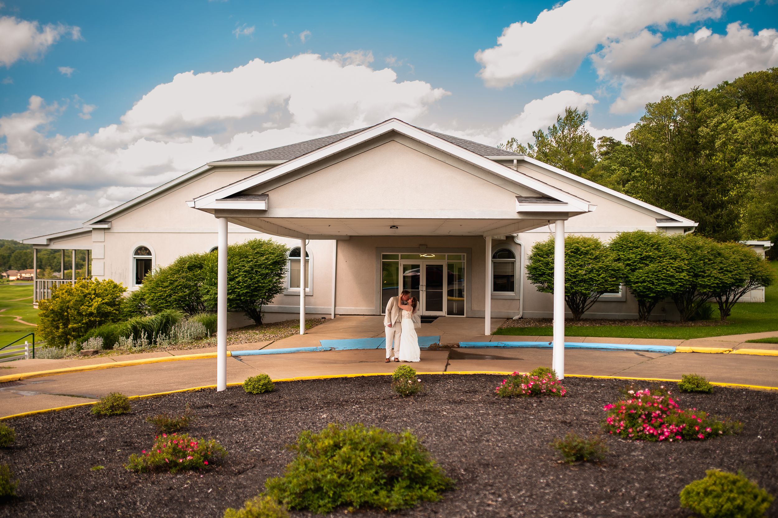 White church building exterior with covered entrance and landscaped garden on sunny day.