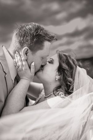 Romantic black and white portrait of newlyweds sharing intimate kiss under flowing veil.