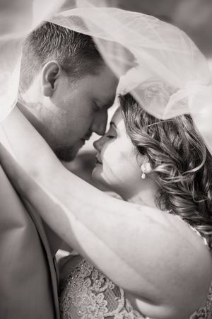 Tender close-up moment between newlyweds with bride's veil flowing in black and white.