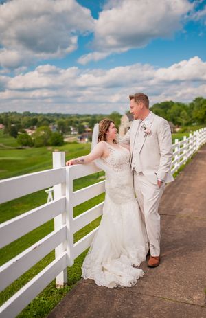 A couple shares a tender moment along a white fence overlooking a scenic countryside.