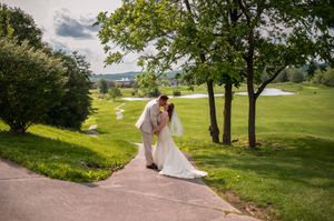 A couple walks down a winding path surrounded by lush green landscaping on their wedding day.
