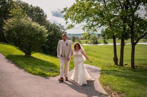 A couple strolls hand in hand along a sunny path with a golf course view.