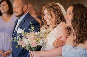 Wedding party members smile while holding pastel floral bouquets.