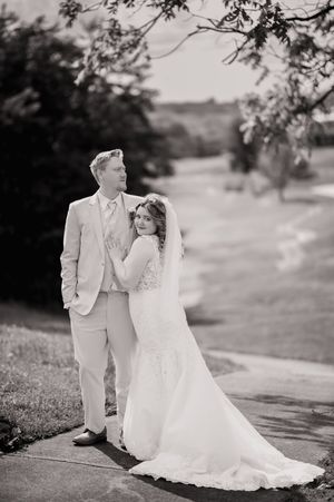 A romantic black and white wedding portrait of a couple posing outdoors in elegant attire.