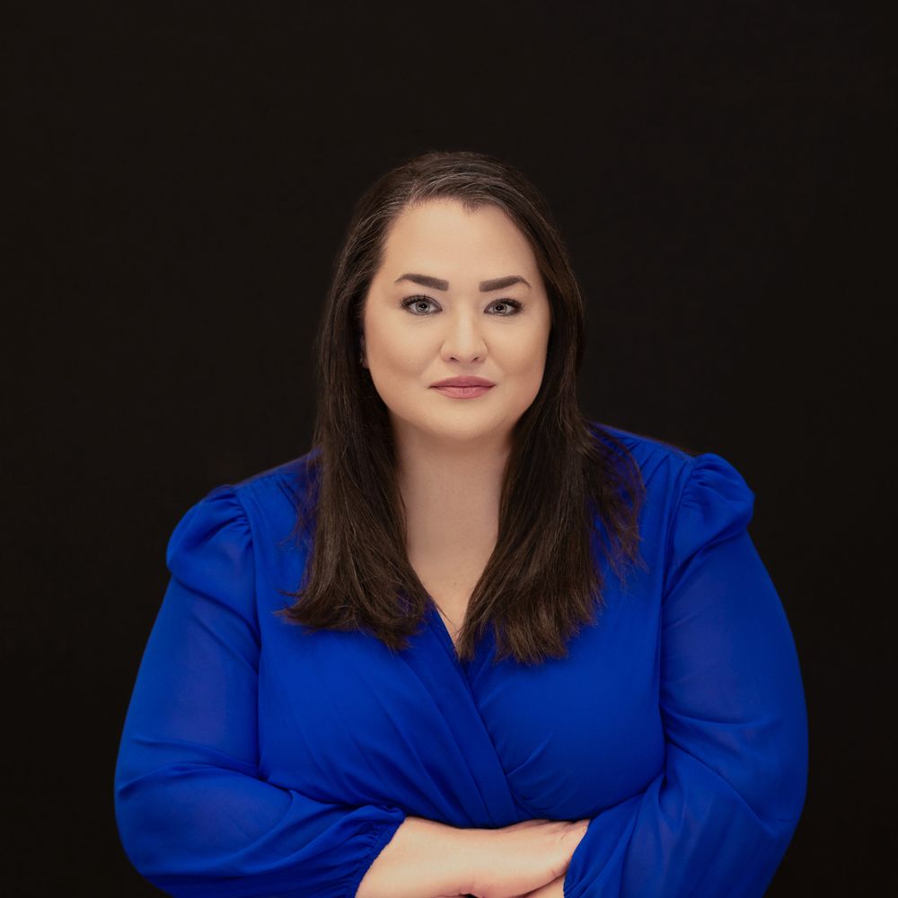 Professional headshot portrait against black background featuring a woman in vibrant royal blue blazer.