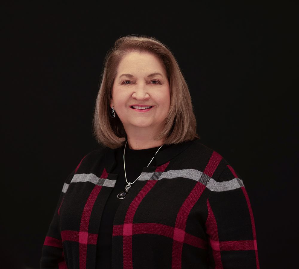 Studio portrait of a woman wearing a red and black buffalo plaid top against dark background.