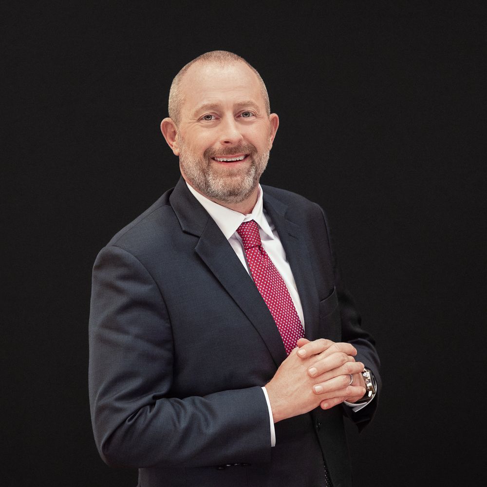 Professional headshot series showing a person in dark suit and burgundy tie against black background.