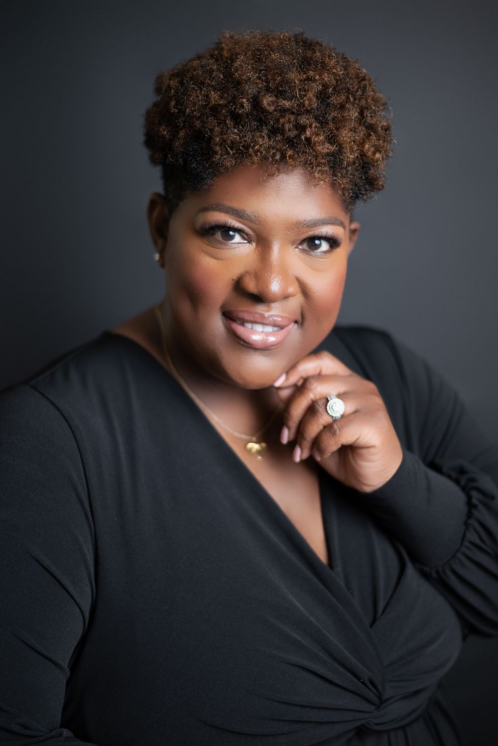 Studio portrait against dark background featuring elegant black wrap dress.