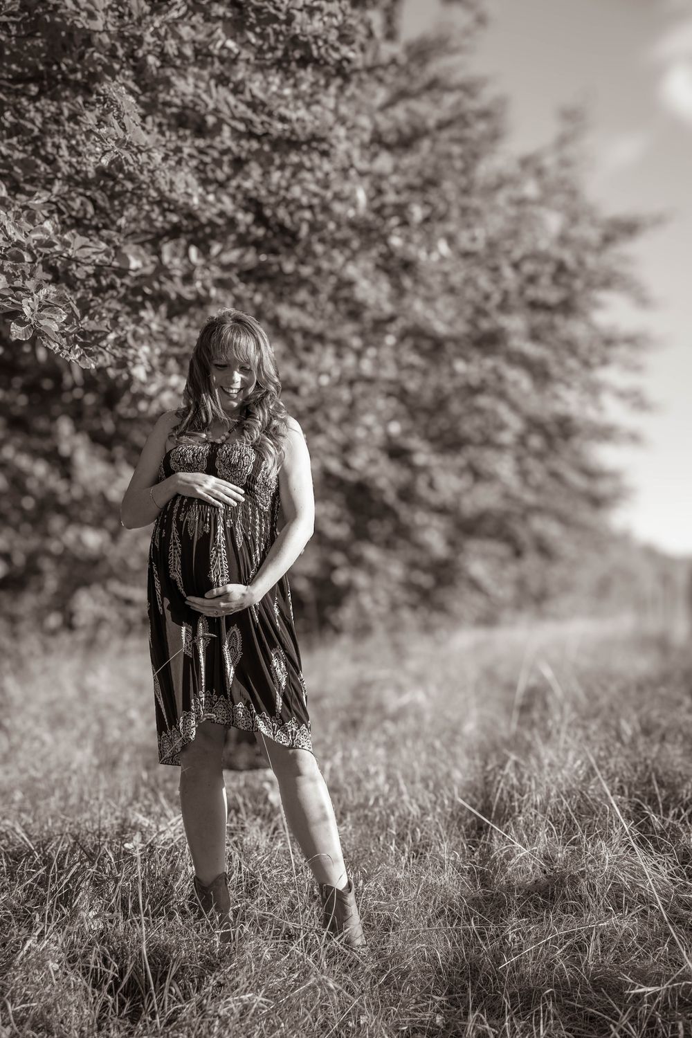 A person in a patterned dress poses in a field during a maternity photoshoot.