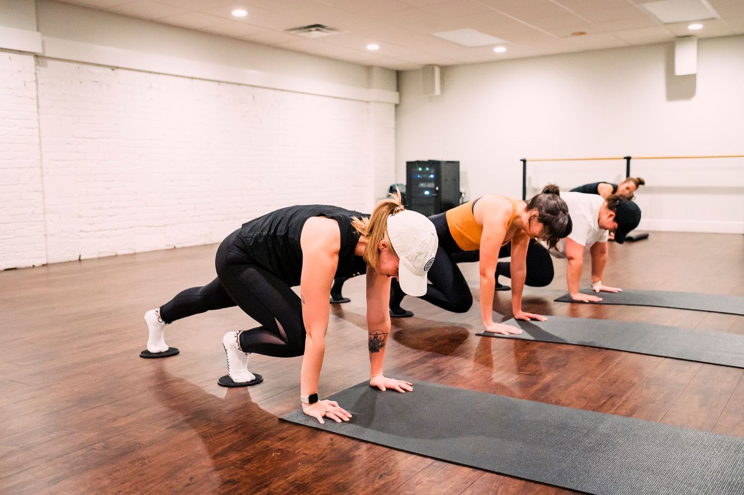 Group of fitness class participants doing mountain climber exercises on yoga mats in a bright studio room.