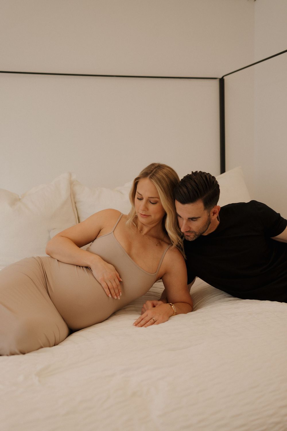 Intimate maternity bedroom photoshoot with couple in neutral tones.