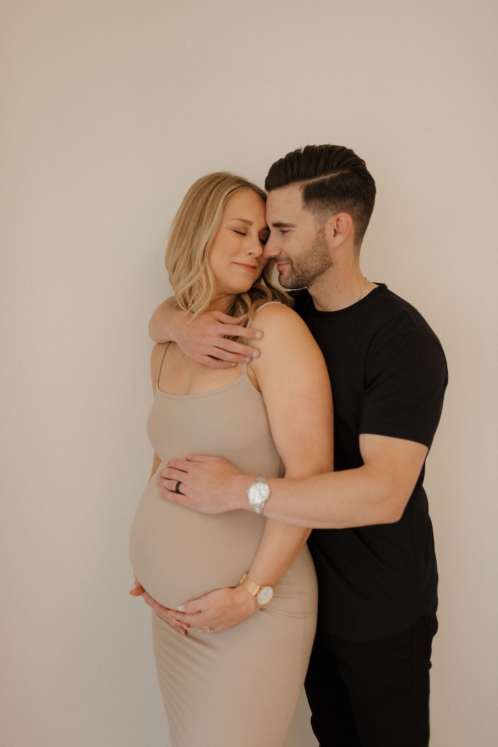 Tender maternity photos of couple in neutral tones against minimal background.