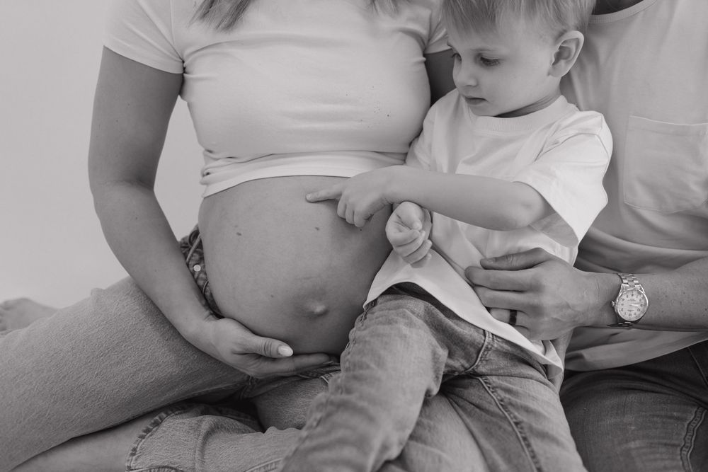 Black and white capture of toddler touching pregnant belly during family maternity session.