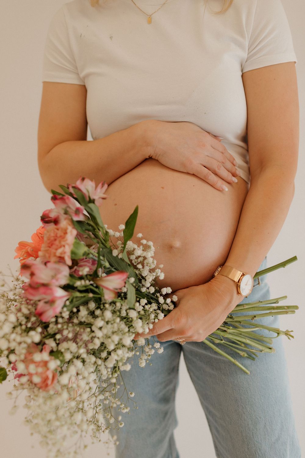 Maternity photo featuring pink flowers and baby's breath against pregnant belly.