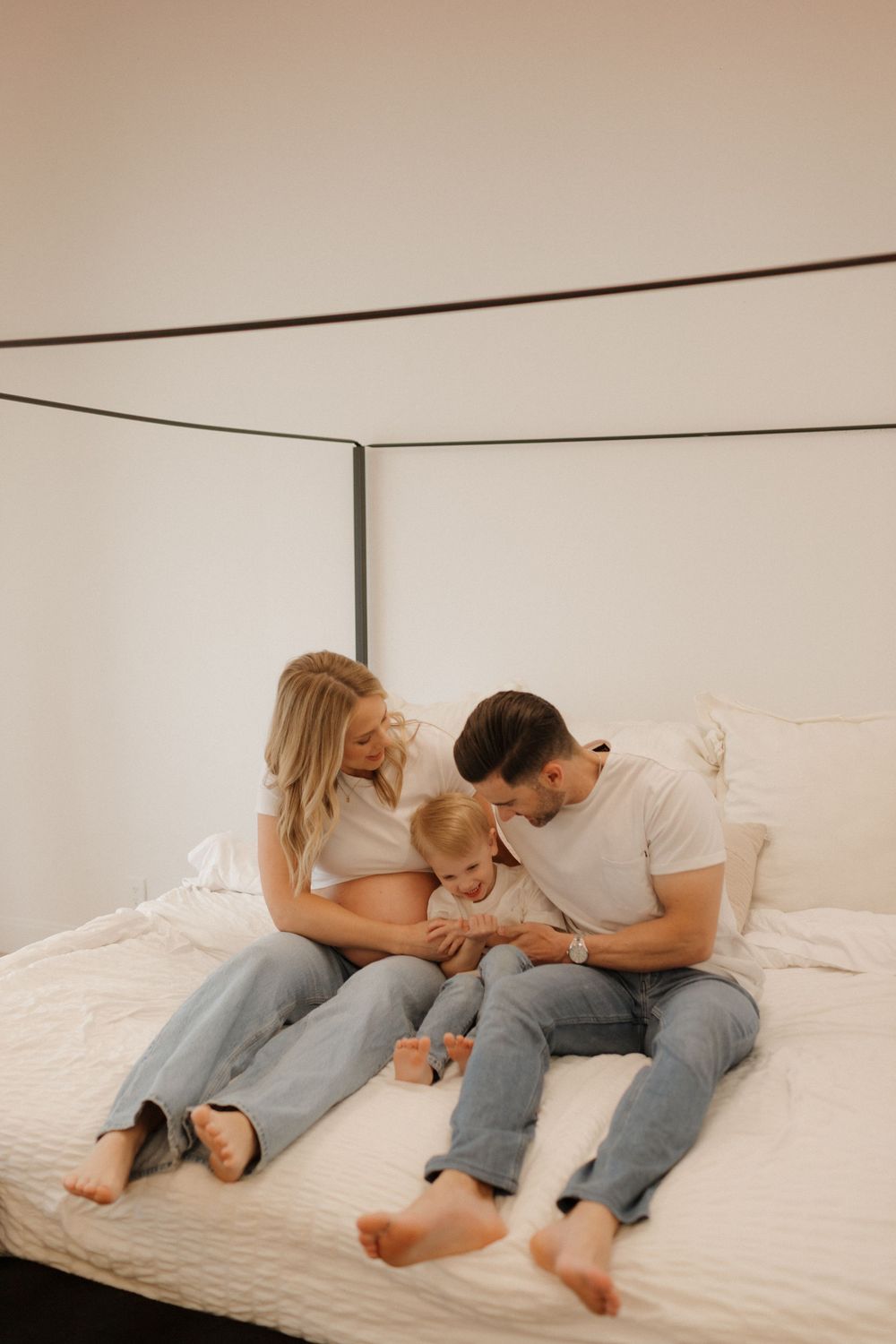 Couple lounging together on white bedding during intimate indoor photoshoot.