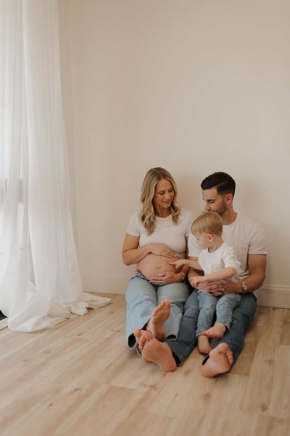 Family sitting on wooden floor sharing intimate moment during maternity photoshoot.