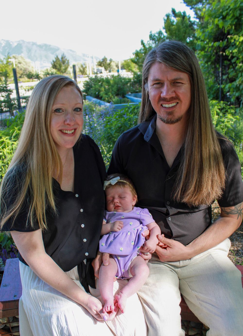 Outdoor family portrait with baby in purple outfit against mountain backdrop.