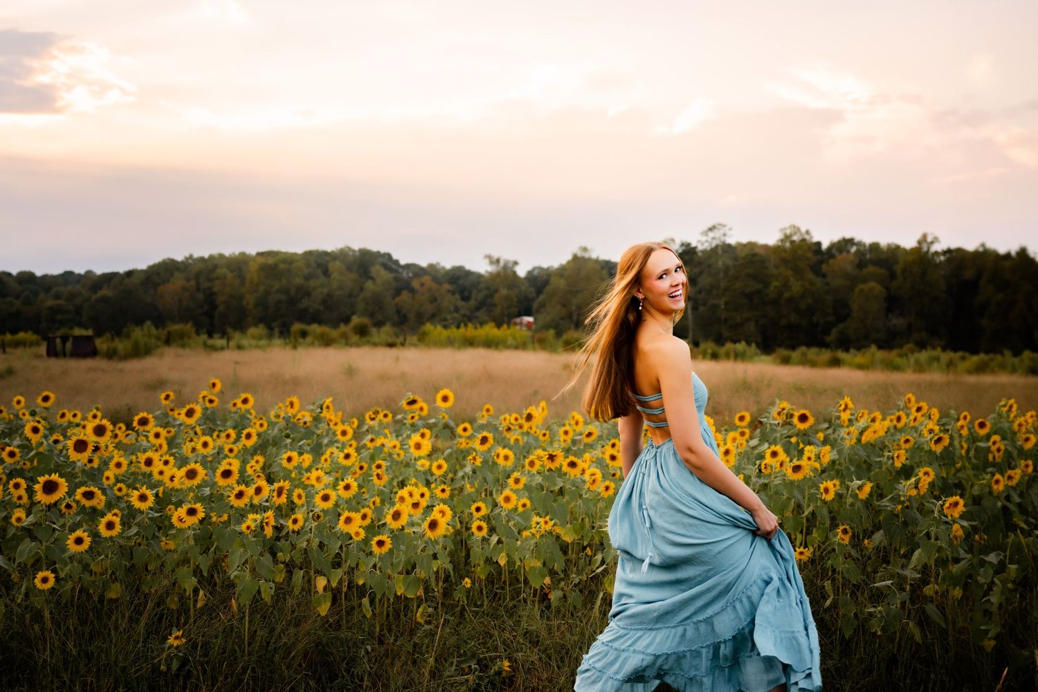 Woman in flowing blue dress twirling in sunflower field at golden hour.