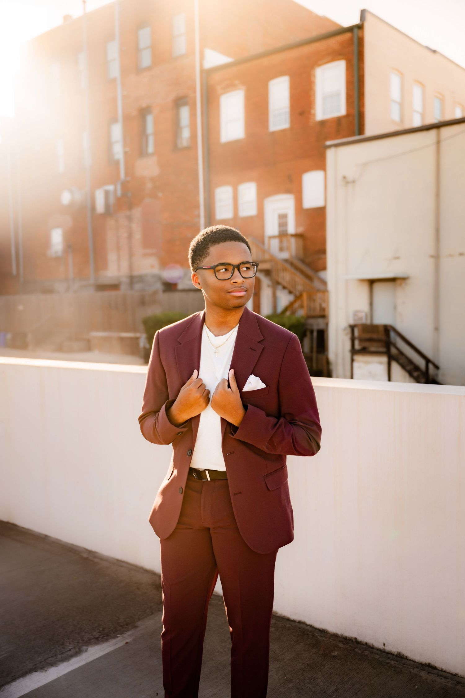 Stylish person in burgundy suit standing against urban backdrop.