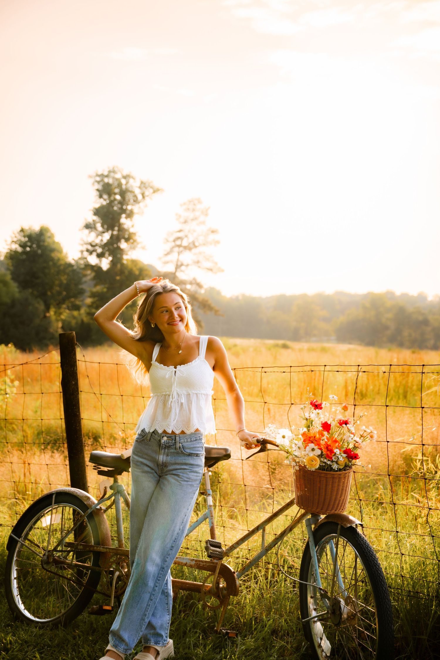 Vintage bicycle with flower basket leans against fence in sunset meadow.