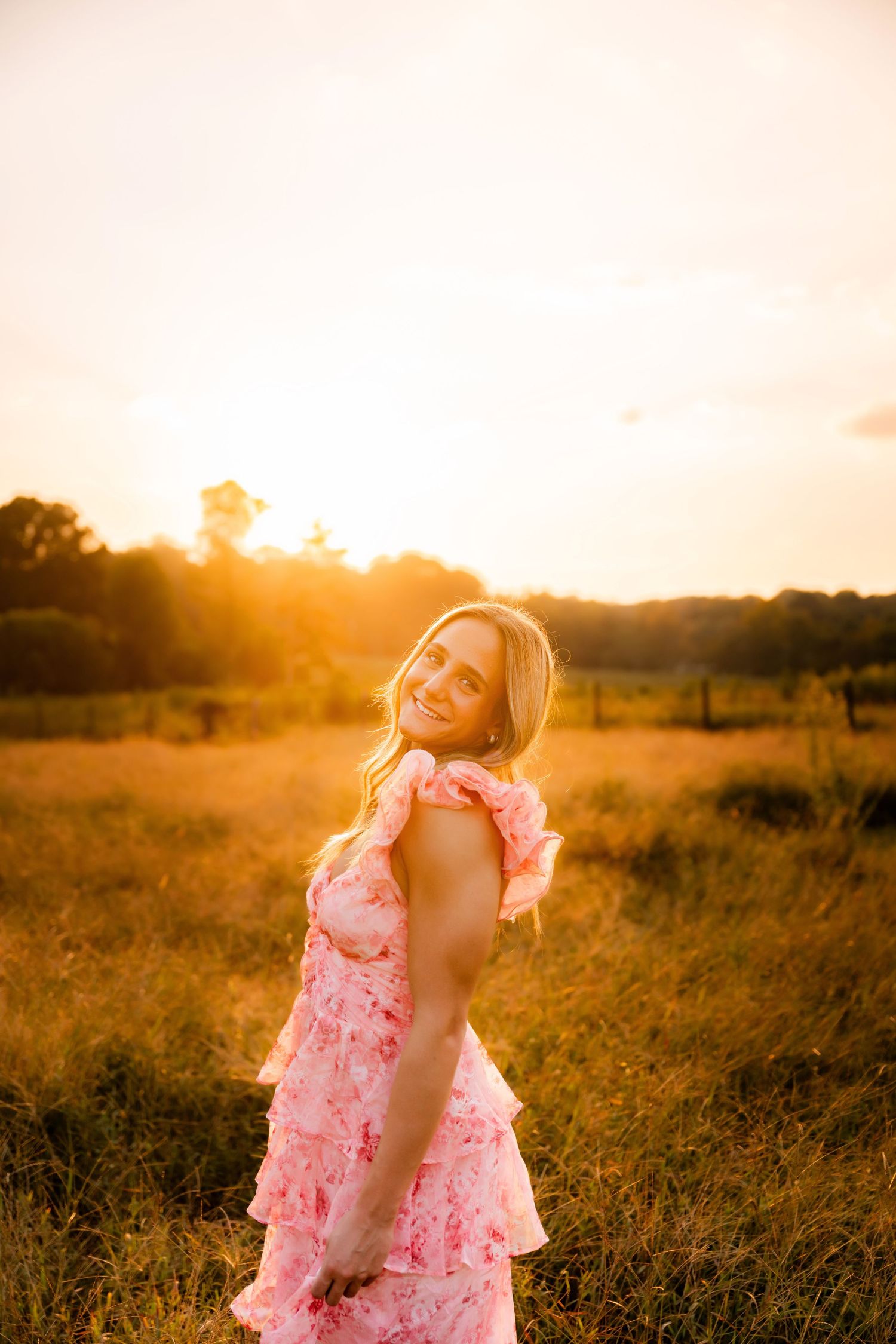 Woman in pink floral dress posing in golden field at sunset.
